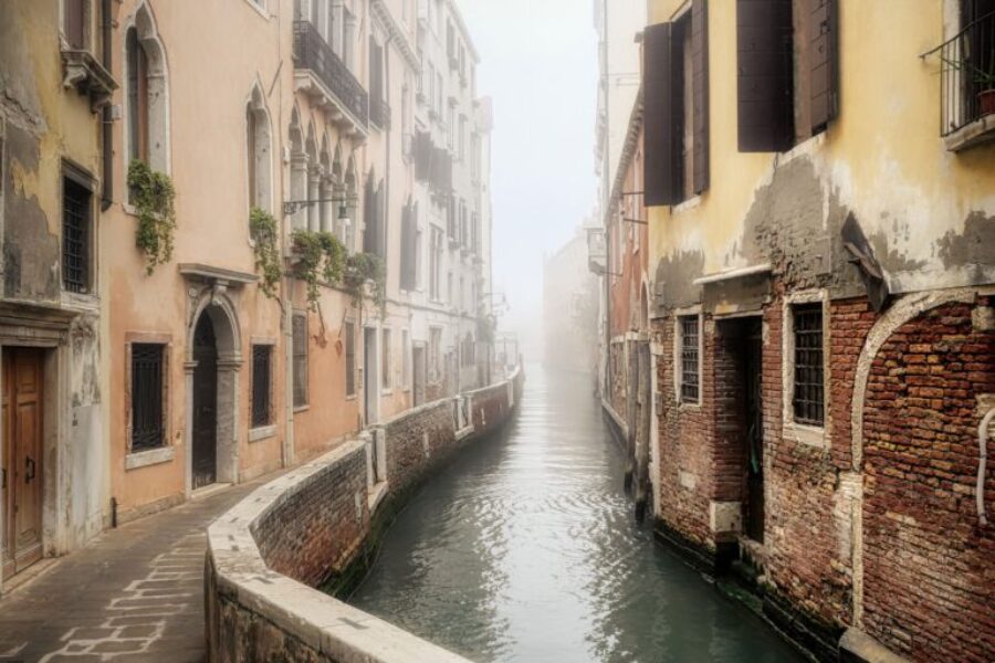 The quiet, narrow back canals of Venice offer a glimpse into the city's atmospheric side, away from the bustling main waterways. Shrouded in morning mist, these "rios" are lined with weathered brick buildings and historic stone arches that have remained unchanged for centuries.