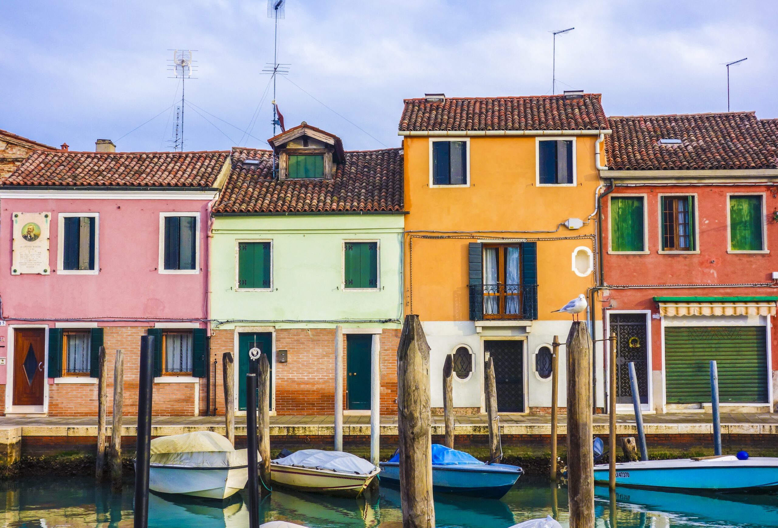 The colorful, sun-drenched houses of Burano, Italy, reflect beautifully off the quiet canal waters. This iconic island is famous for its bright facades and charming, small-town atmosphere.